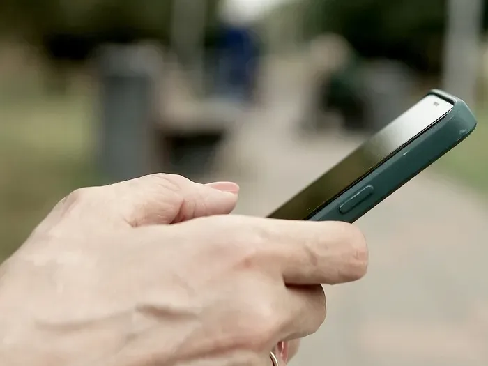 Hands holding a smartphone outdoors, showing mobile search and contact for local businesses on City Bizz One